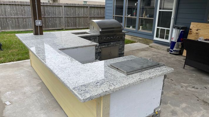 Outdoor backyard with a white stone island, built-in grill, and covered sink area beside a patio and house