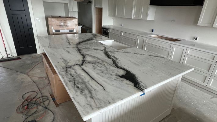 Kitchen with large white marble island and dark gray veining, white cabinets, and unfinished floor work