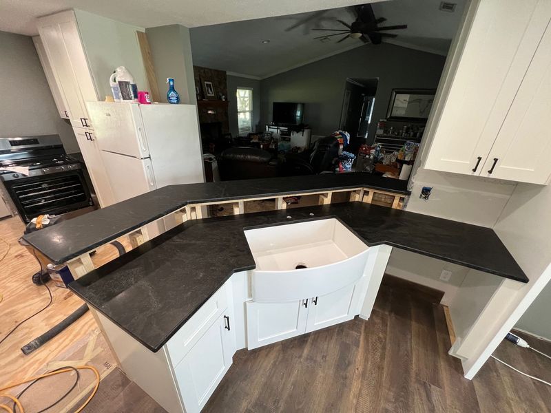 U-shaped kitchen with black countertops, white cabinets, and a central island under renovation