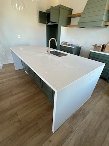 Modern kitchen with a large white island, sink, and dark cabinets with wood floors
