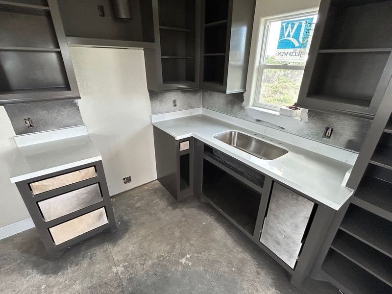 Unfinished kitchen with dark cabinets, light countertops, sink, and a window over the counter.