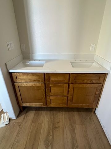 Wooden double vanity with white countertop and two sinks in a small bathroom alcove.