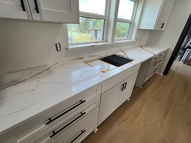 White kitchen with marble-look countertops, black hardware, window sink, and light wood floors