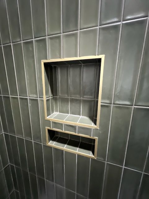 Black tiled wall with a recessed metal service opening and small lower slot.