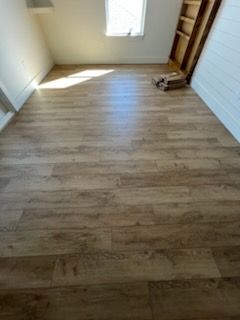Small empty room with light wood flooring, white walls, and sunlight from a window.