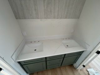 Bathroom vanity with double sinks, green cabinets, and a light wood ceiling underneath a sloped wall