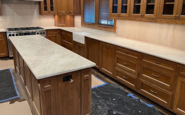 Wooden kitchen with long island, beige countertops, and built-in cabinets and windows.