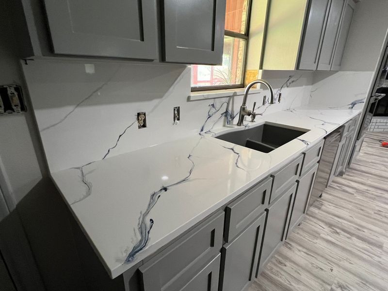 Damaged kitchen countertop with large cracks, near a sink and gray cabinets