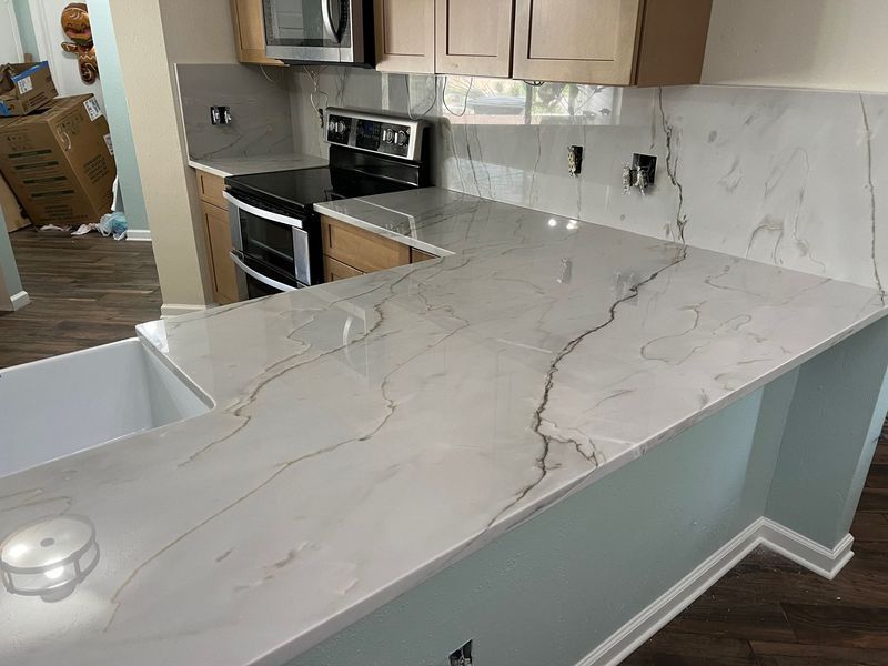 Kitchen with white marble-look island countertop, light wood cabinets, and stainless steel stove and microwave.