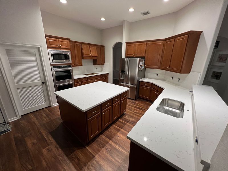 Modern kitchen with wood cabinets, white countertops, stainless appliances, and a center island