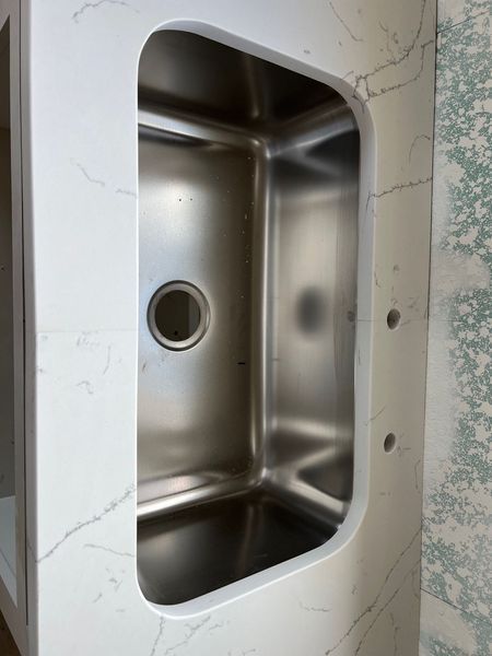 Stainless steel sink basin set into a white marble countertop with a circular drain opening