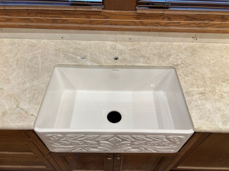 White rectangular bathroom sink with a black drain set into a beige tiled wall and wooden vanity.