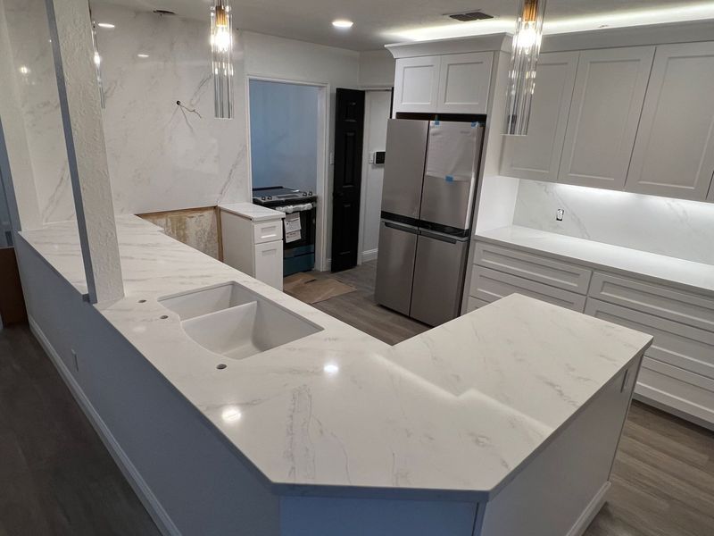 Modern white kitchen with marble island, stainless steel fridge, and pendant lights