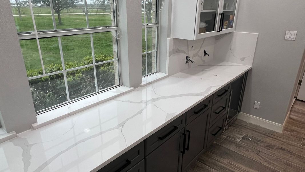 Long white countertop with dark cabinets beside large windows in a bright room