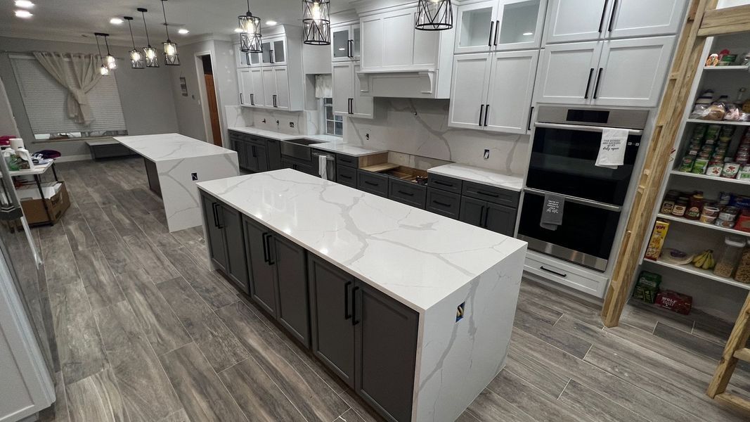 Modern kitchen with white cabinets, gray island, and wood-look flooring in a bright showroom