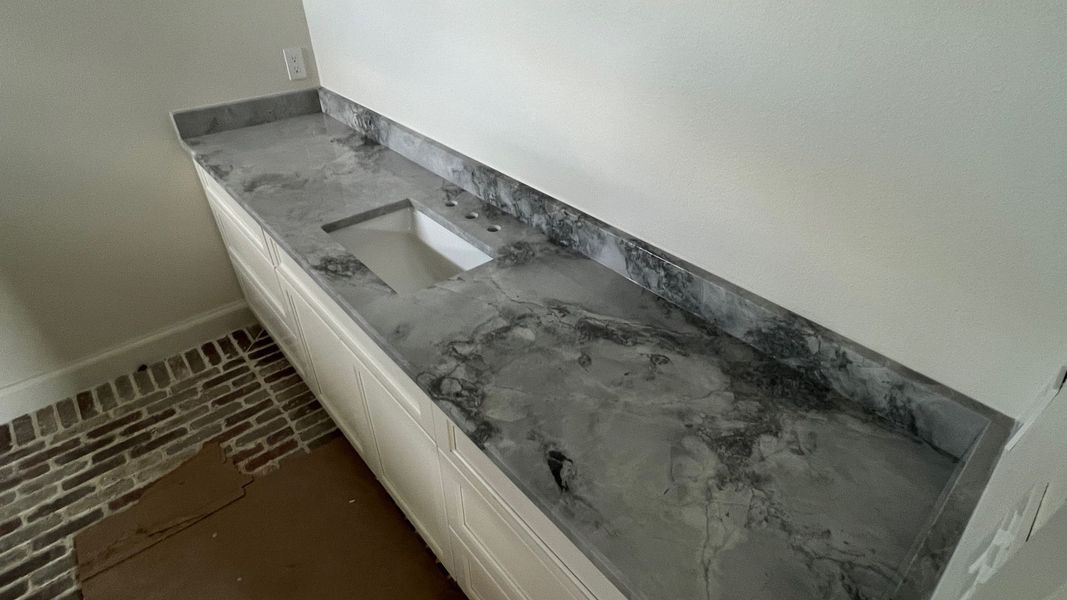 Gray marble bathroom vanity with built-in sink and white cabinets beneath, against a white wall.