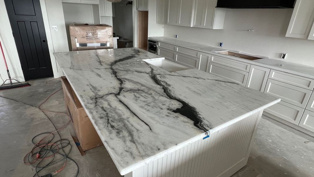 Marble-look kitchen island countertop with black veining in a modern white kitchen under construction