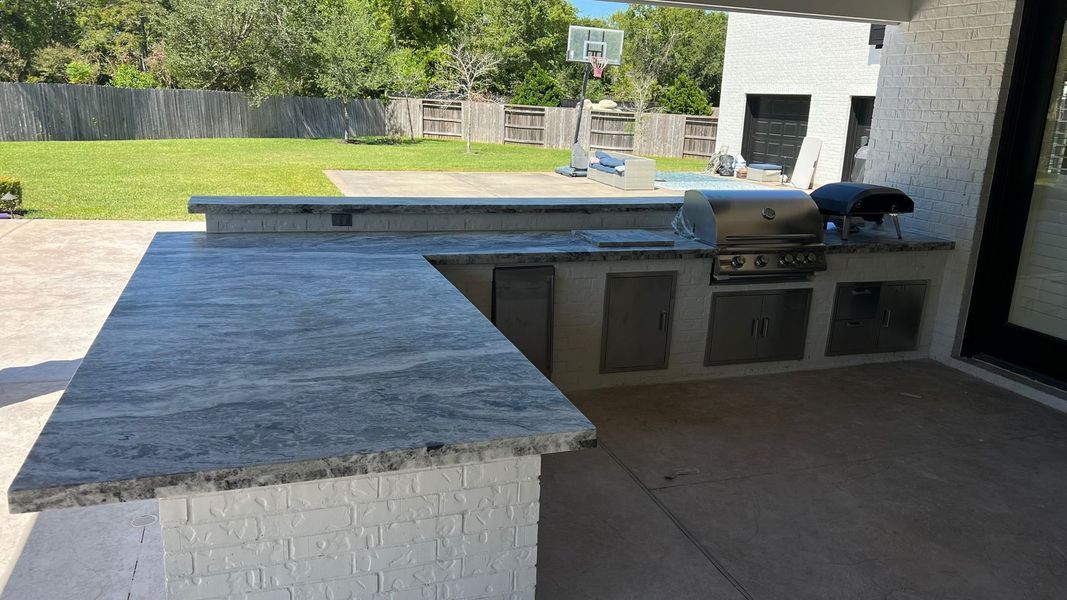 Outdoor patio with granite countertops, built-in cabinets, grill, and a green backyard beyond.