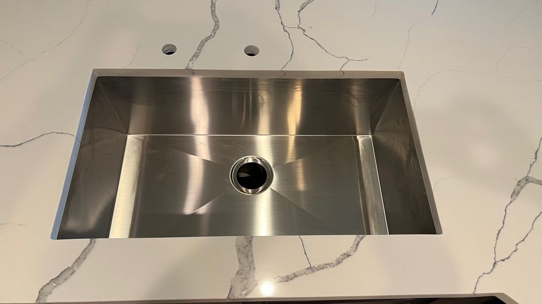 Stainless steel kitchen sink set in a white marble countertop with gray veining.