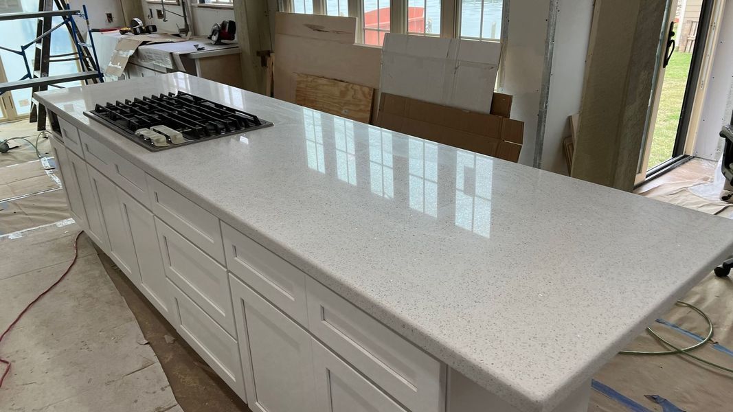 Long white kitchen island with speckled countertop and built-in cooktop in a bright room