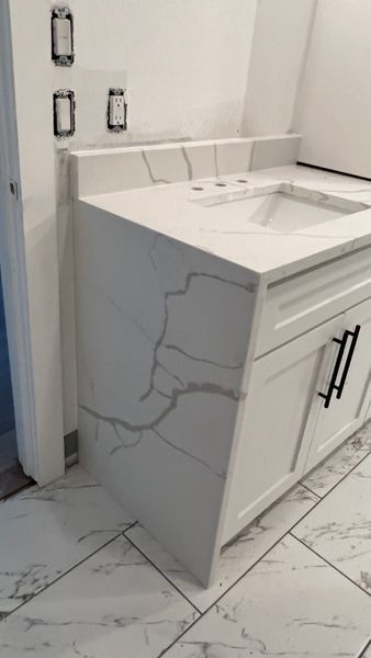 Modern bathroom vanity with white marble countertop and sink, black handles, and cracked side panel near tiled floor