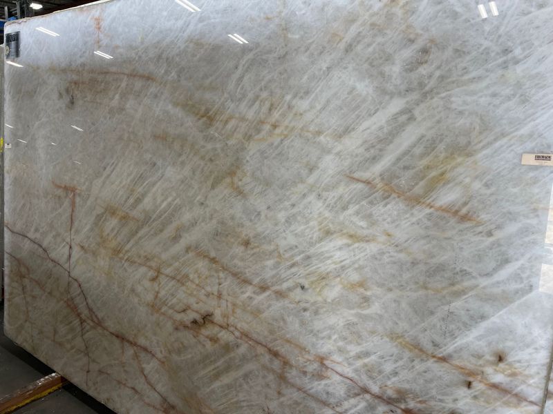 Large polished beige marble slab with subtle gray and brown veining, leaning upright in a warehouse.