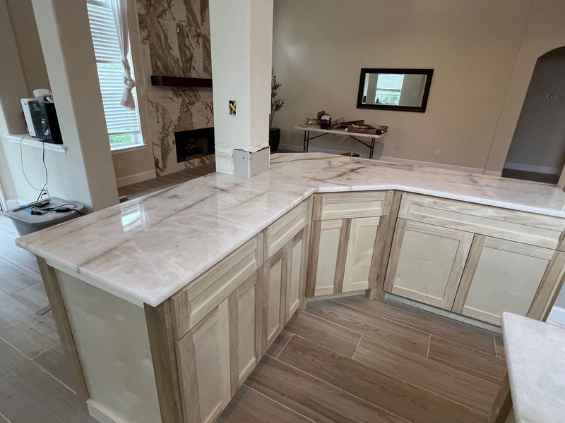Empty kitchen with light wood cabinets, marble countertops, and a breakfast bar.