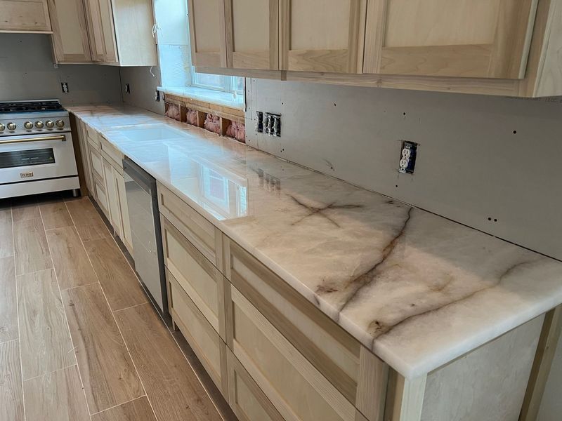 Partially renovated kitchen with light wood cabinets, marble-look countertop, and unfinished backsplash areas