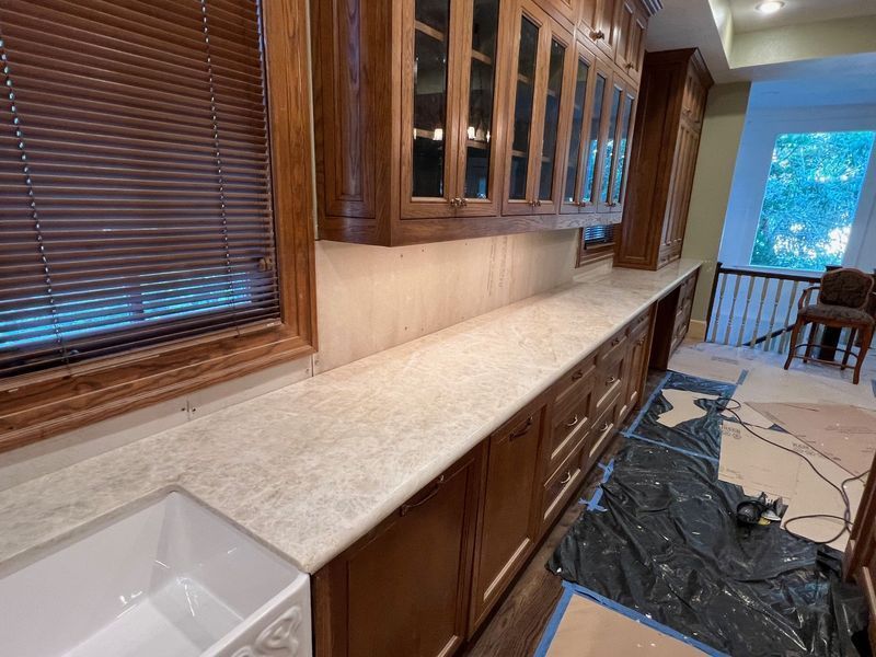 Kitchen with long beige countertop, wooden cabinets, window blinds, and a floor covered in protective plastic.