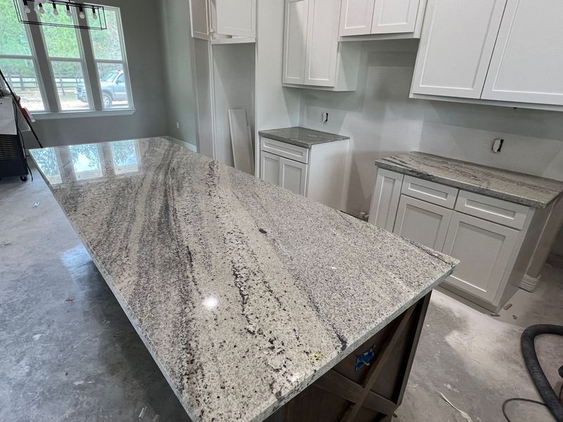Kitchen island with a speckled granite countertop in an unfinished bright kitchen
