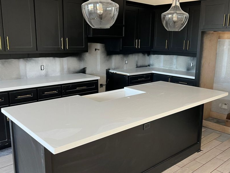 Modern kitchen with black cabinets, white island countertop, and pendant lights