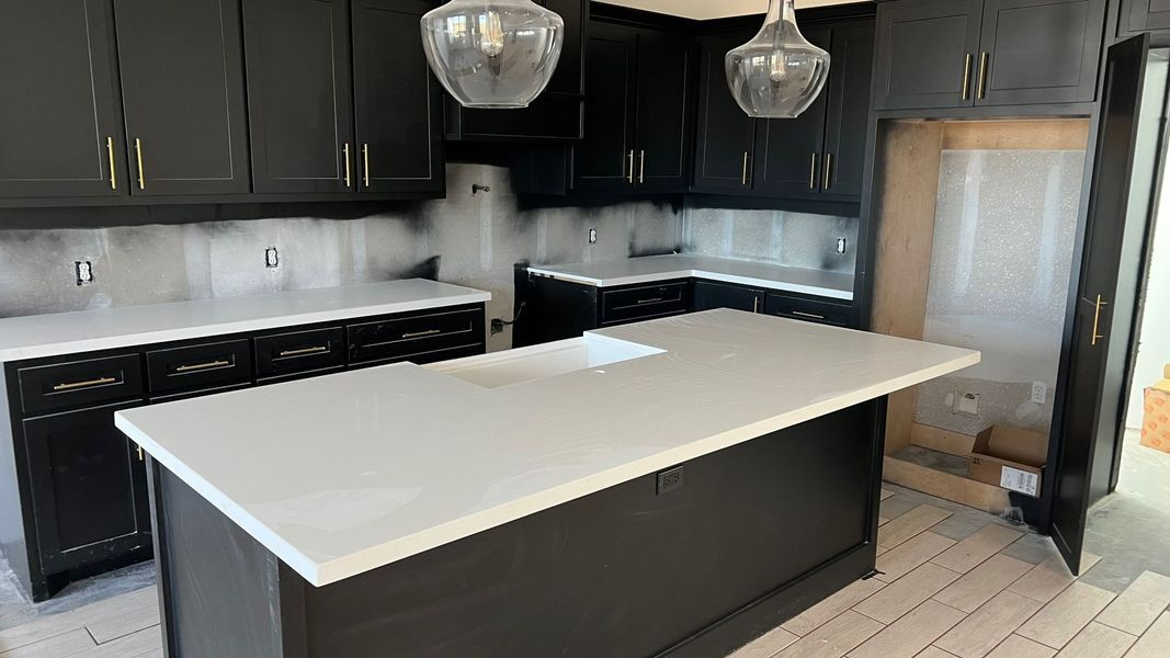 Modern kitchen with black cabinets, white countertops, stainless refrigerator, and a large island