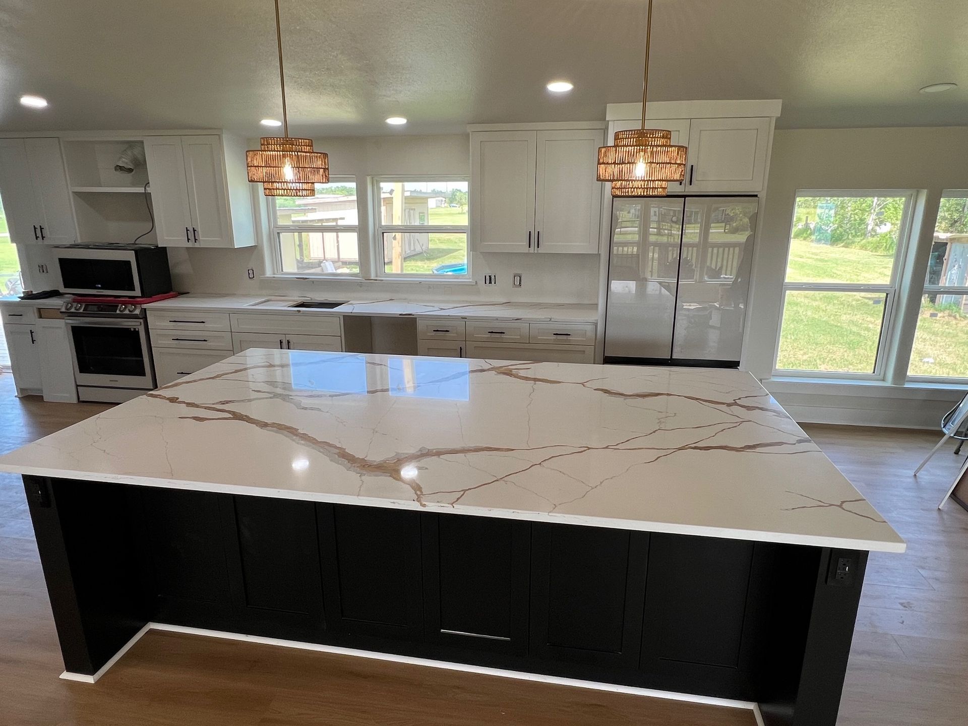 Modern kitchen with white cabinets, large marble island, pendant lights, and bright windows