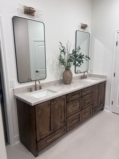 Double vanity bathroom with dark wood cabinets, white countertops, mirrors, and a vase of greenery