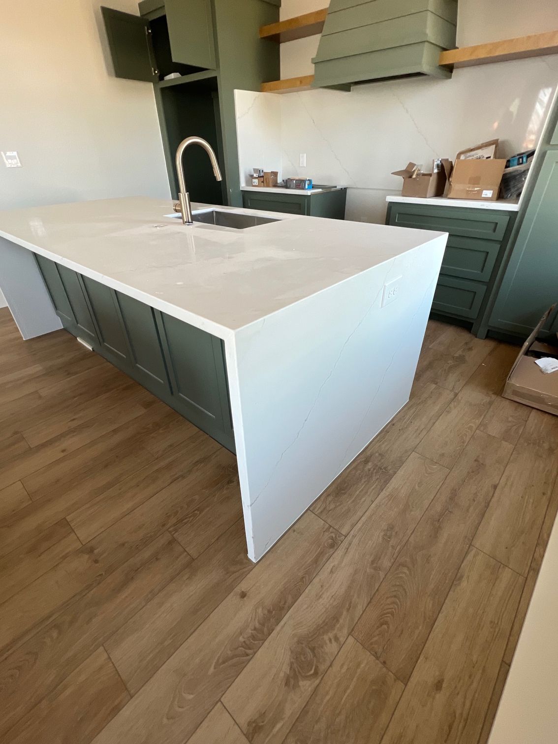 Modern kitchen with a white island, dark green cabinets, and wood flooring