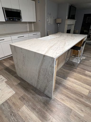 Large marble kitchen island in a modern kitchen with white cabinets and wood flooring