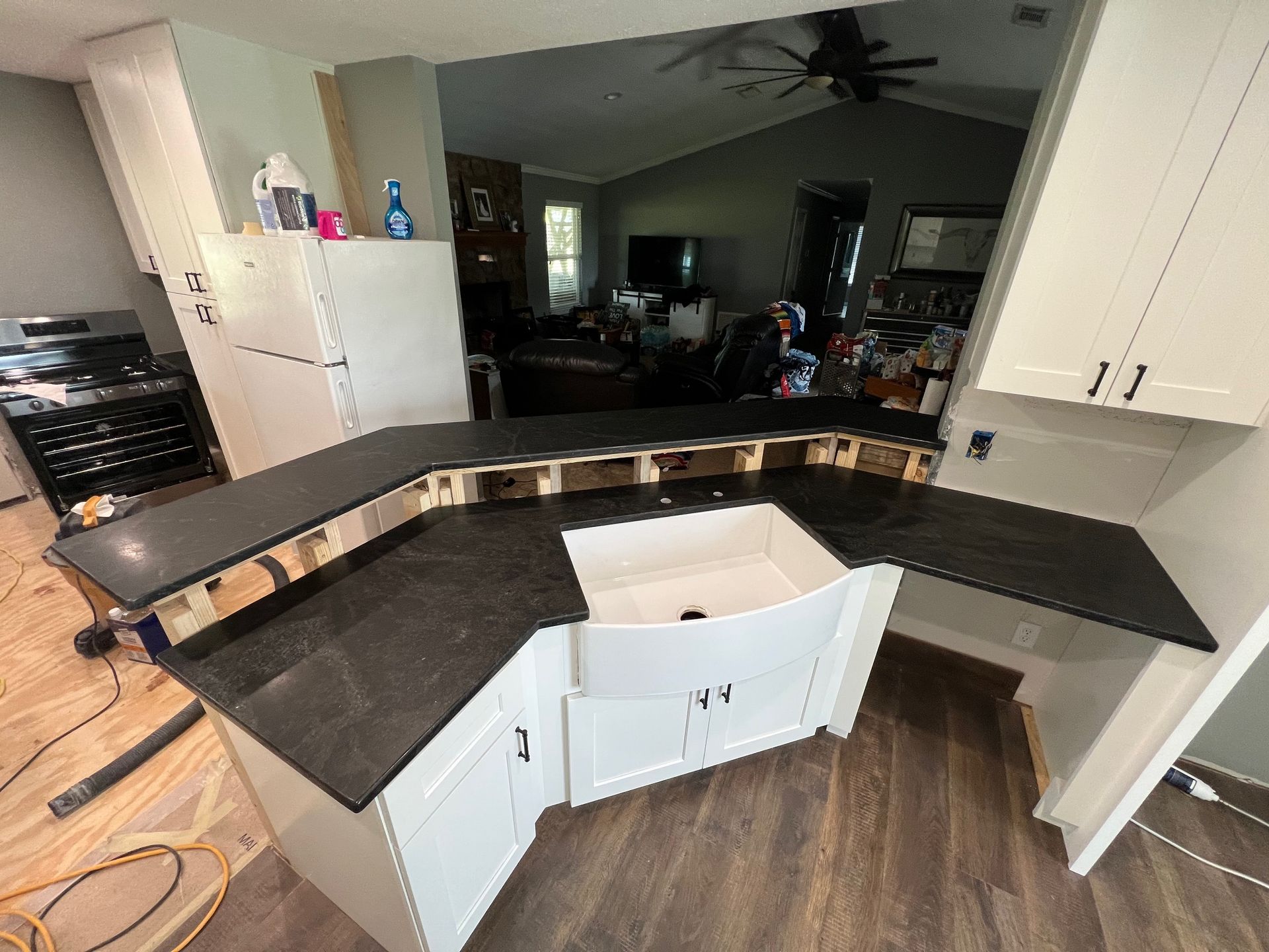 Kitchen under renovation with dark countertops, white cabinets, and open lower cabinet doors
