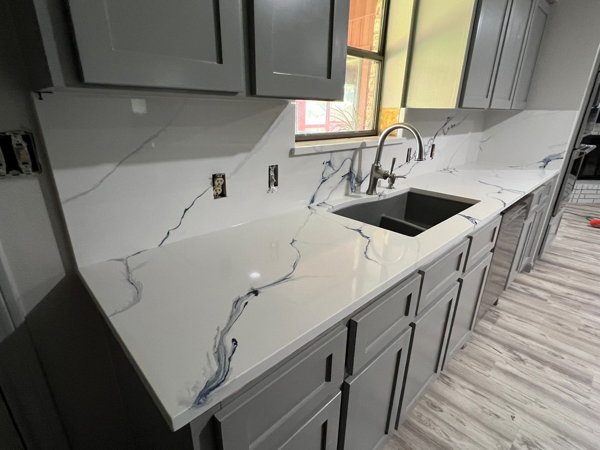 Kitchen countertop with visible crack damage, gray cabinets, sink, and window above.