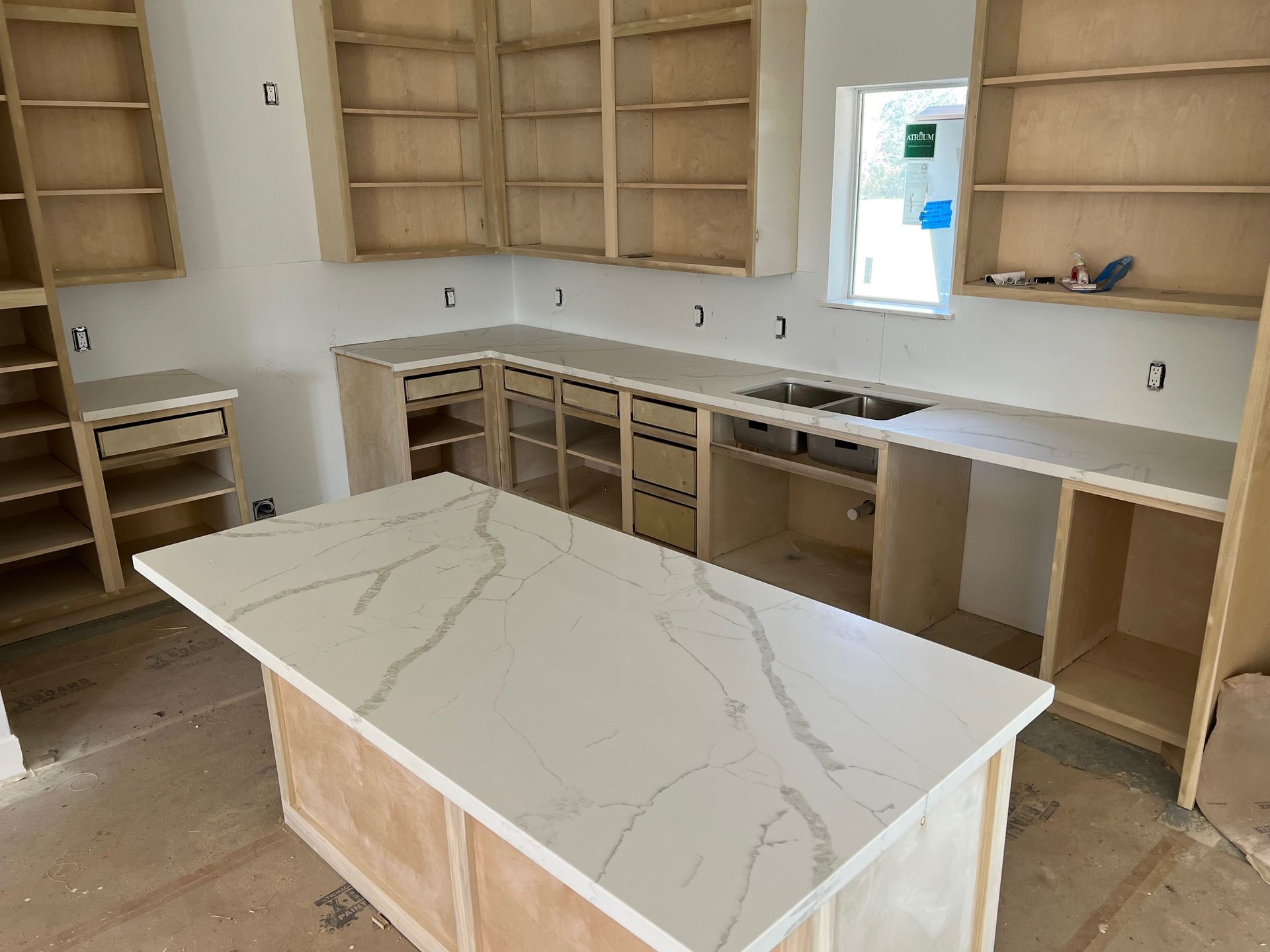 Unfinished kitchen with white cabinets, marble island, and open shelving under construction