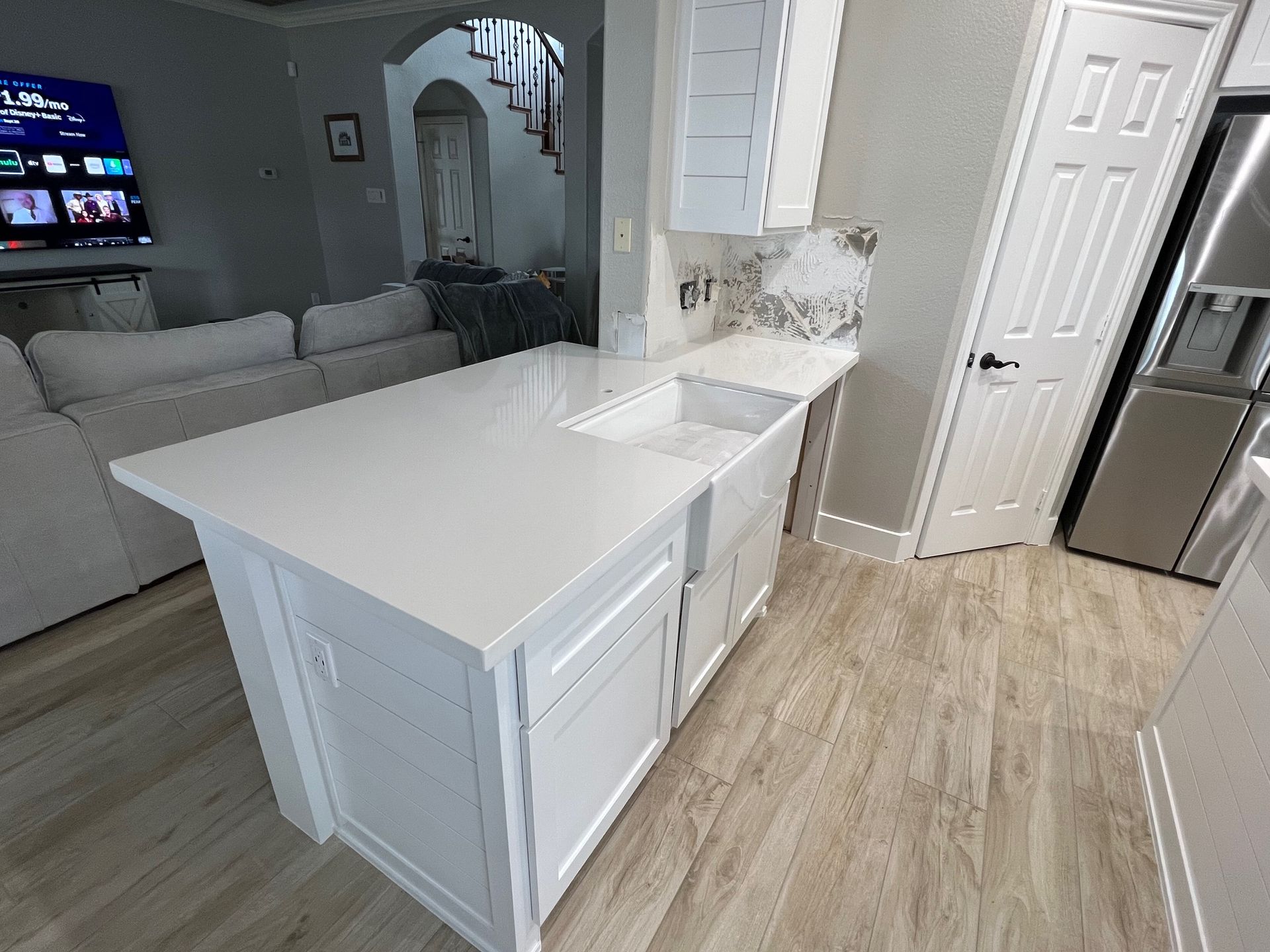 Bright modern kitchen with white island, light wood flooring, and gray living room visible beyond.