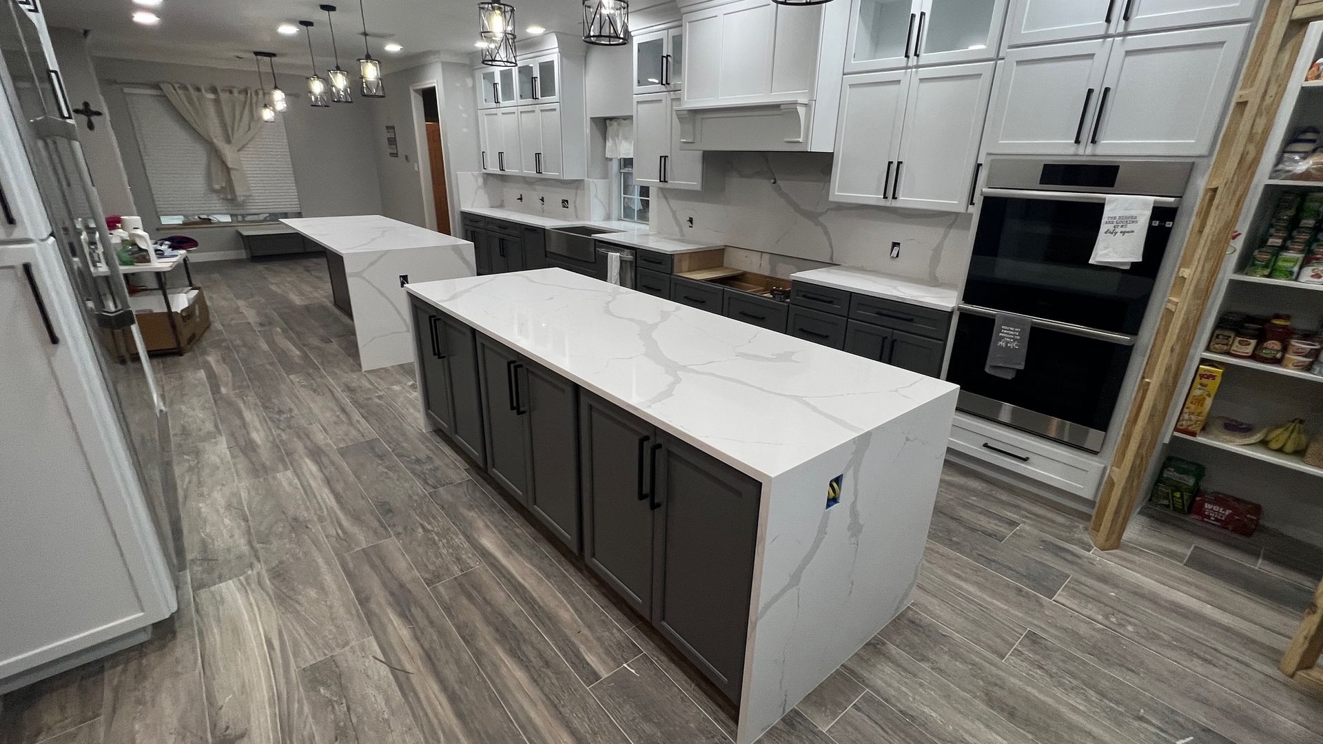 Modern kitchen with white cabinets, marble island, dark lower drawers, and wood-look flooring