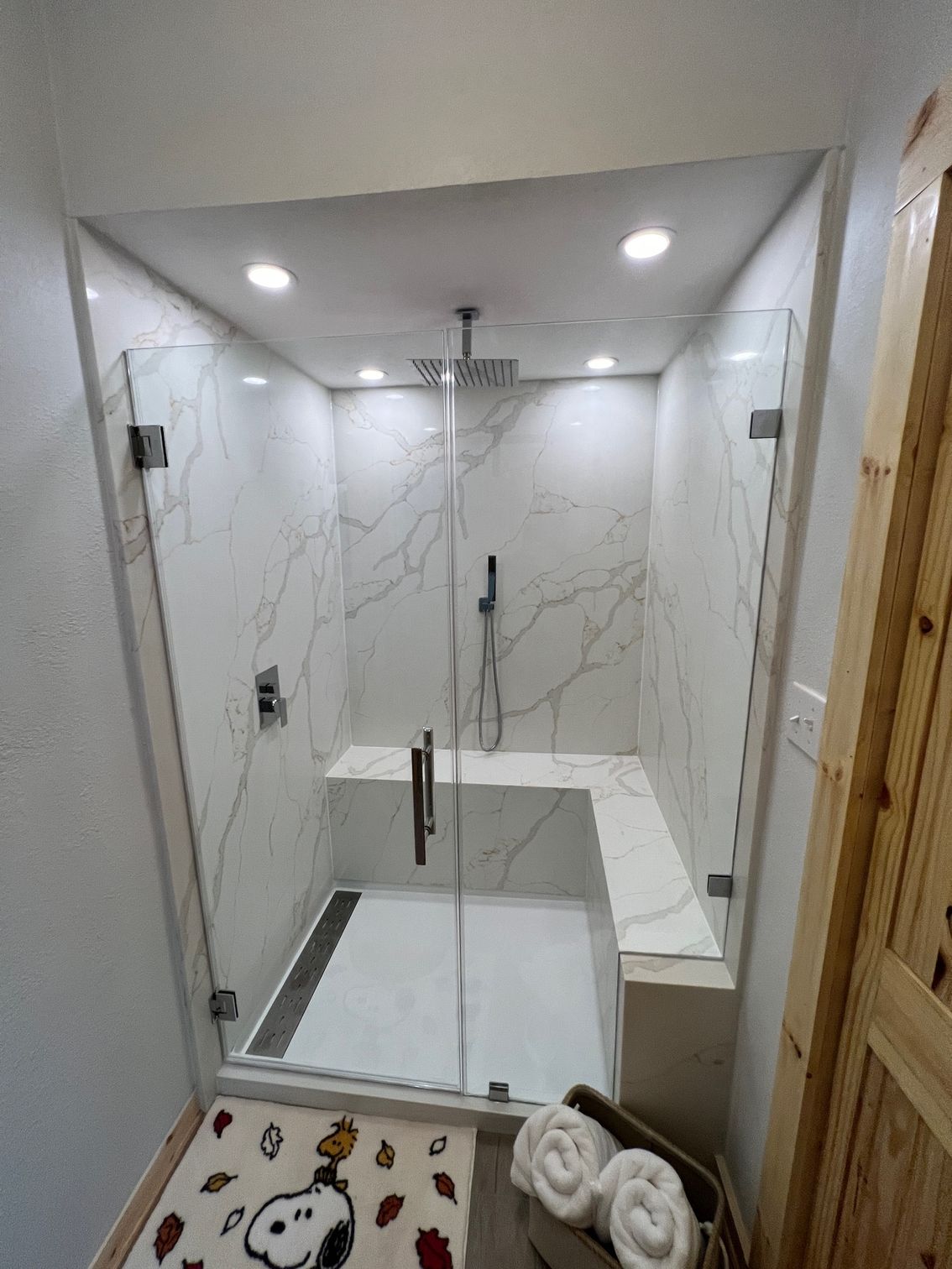 Glass-enclosed shower with white marble tile, built-in bench, and chrome fixtures