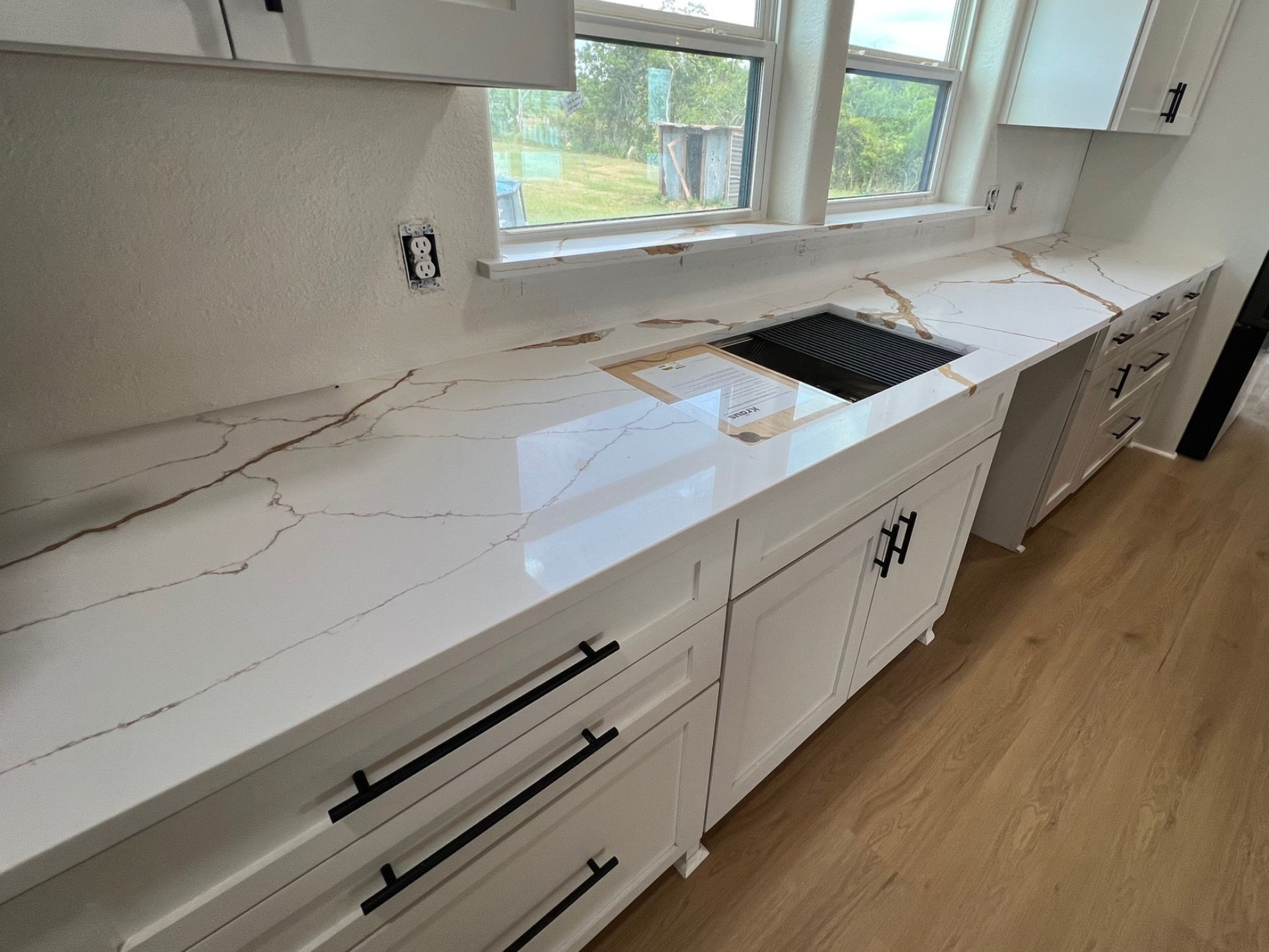 White kitchen countertop with sink cutout, drawers, and window above wooden floor