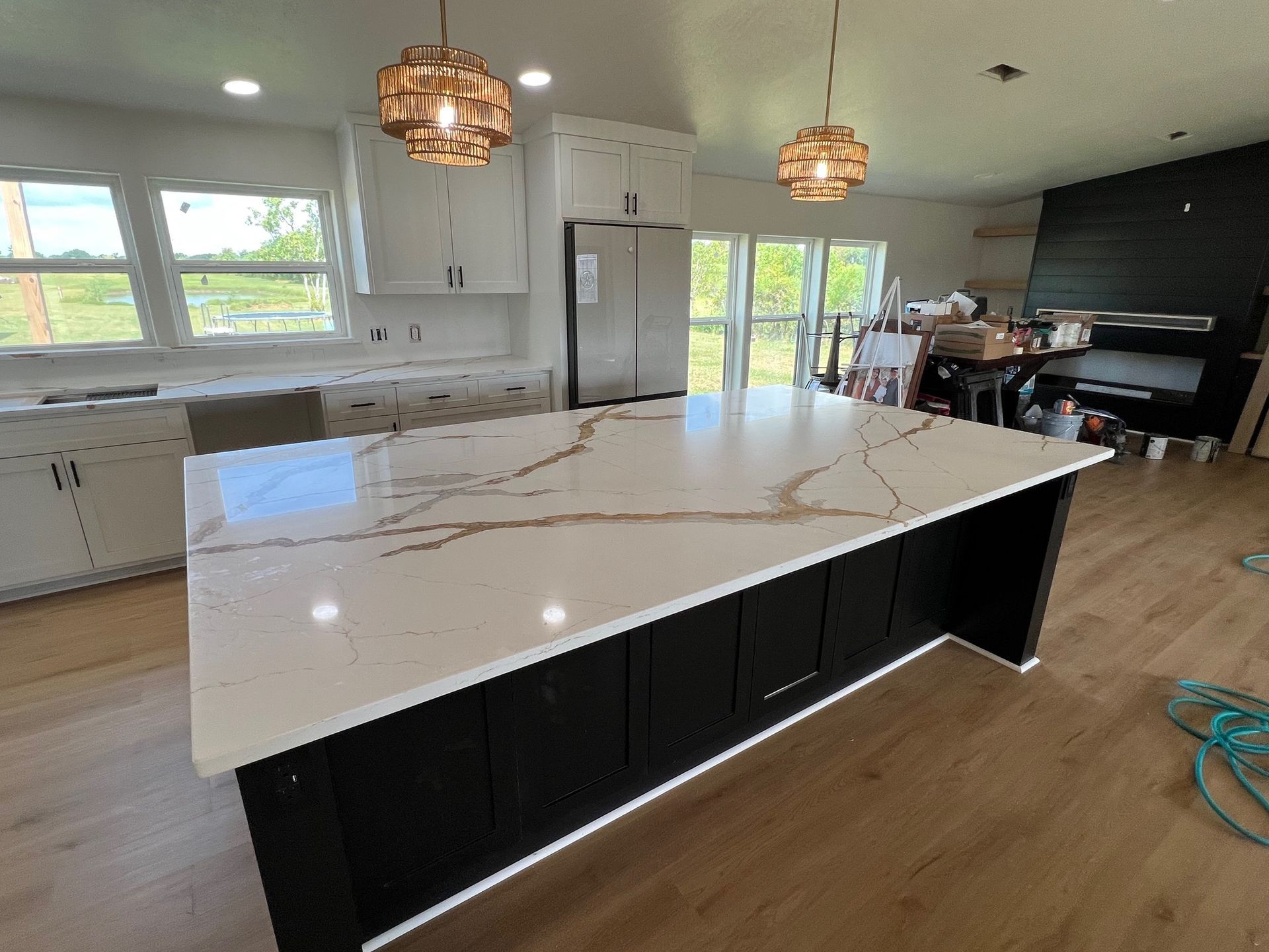 Modern kitchen with large white island, black cabinets, wood floors, and pendant lights