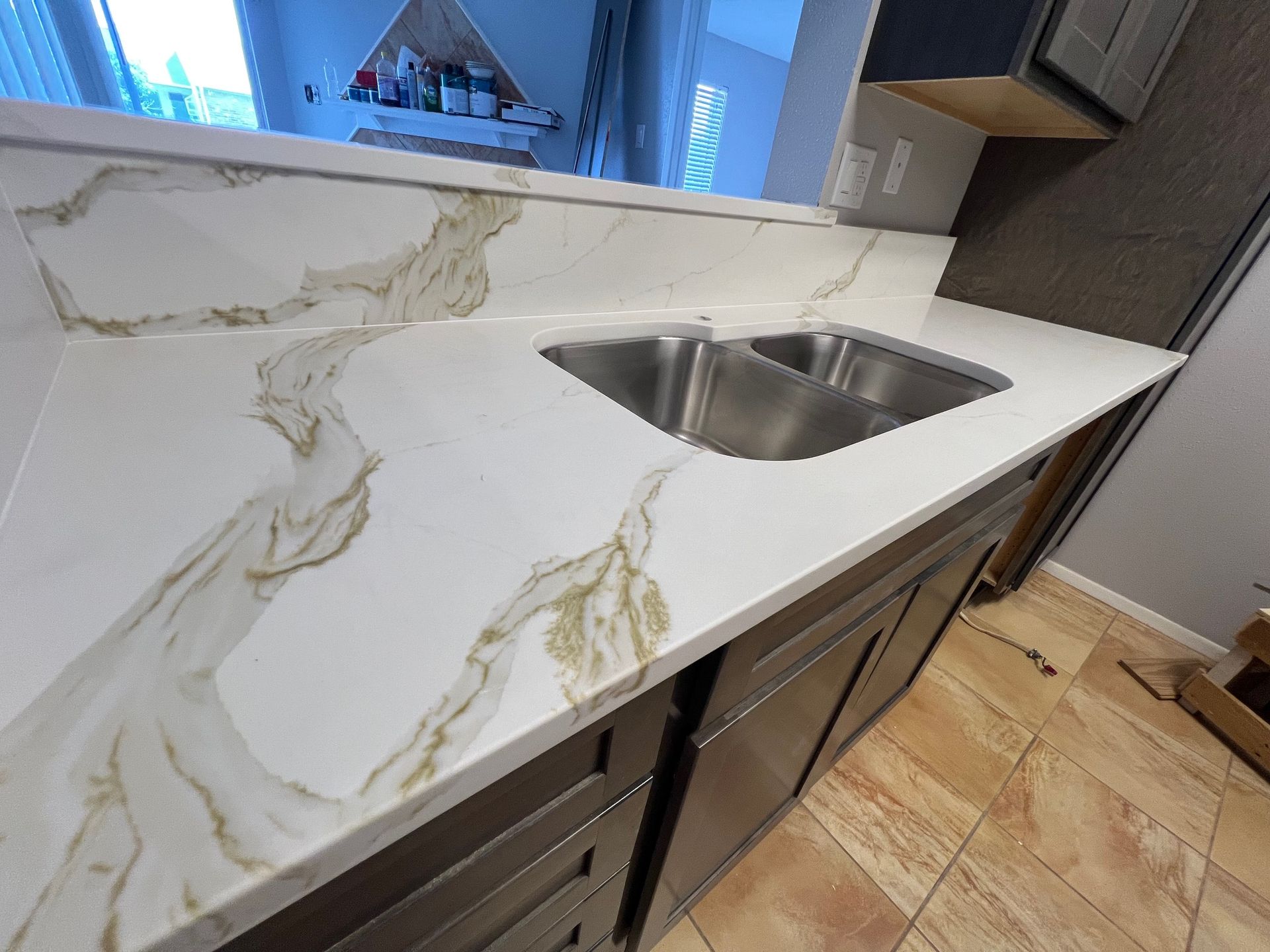 Modern kitchen counter with white marble-look surface and stainless steel sink, with floor finishing in progress