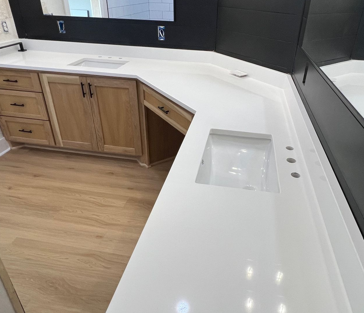 Modern kitchen with white countertop, wood cabinets, integrated sink, and a large mirror wall.