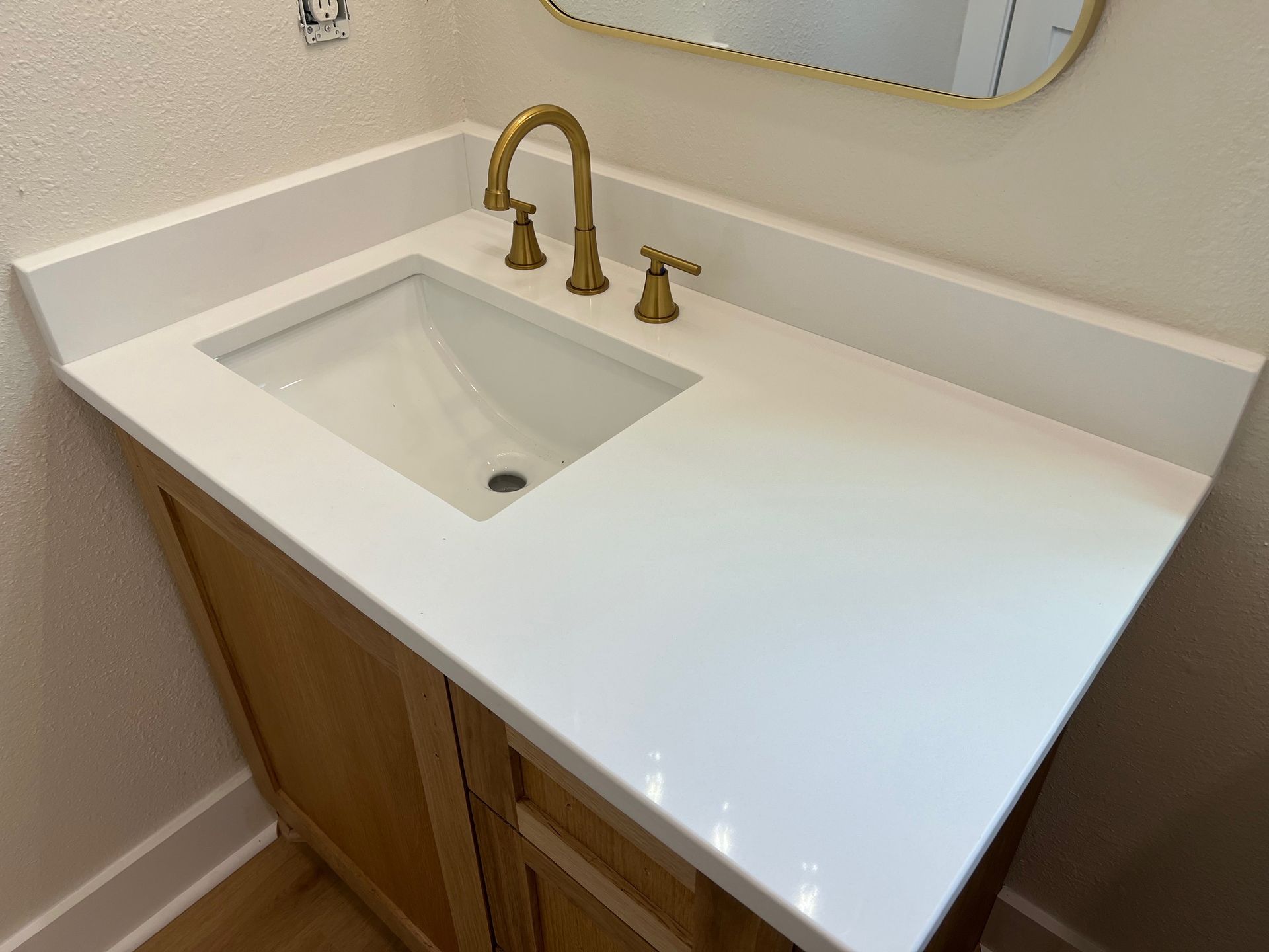 White bathroom vanity with gold faucet and built-in sink under a mirror