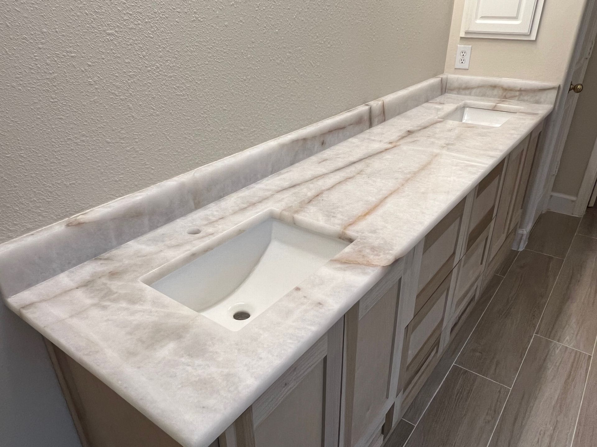 Long bathroom vanity with a white marble countertop and single sink against a beige wall