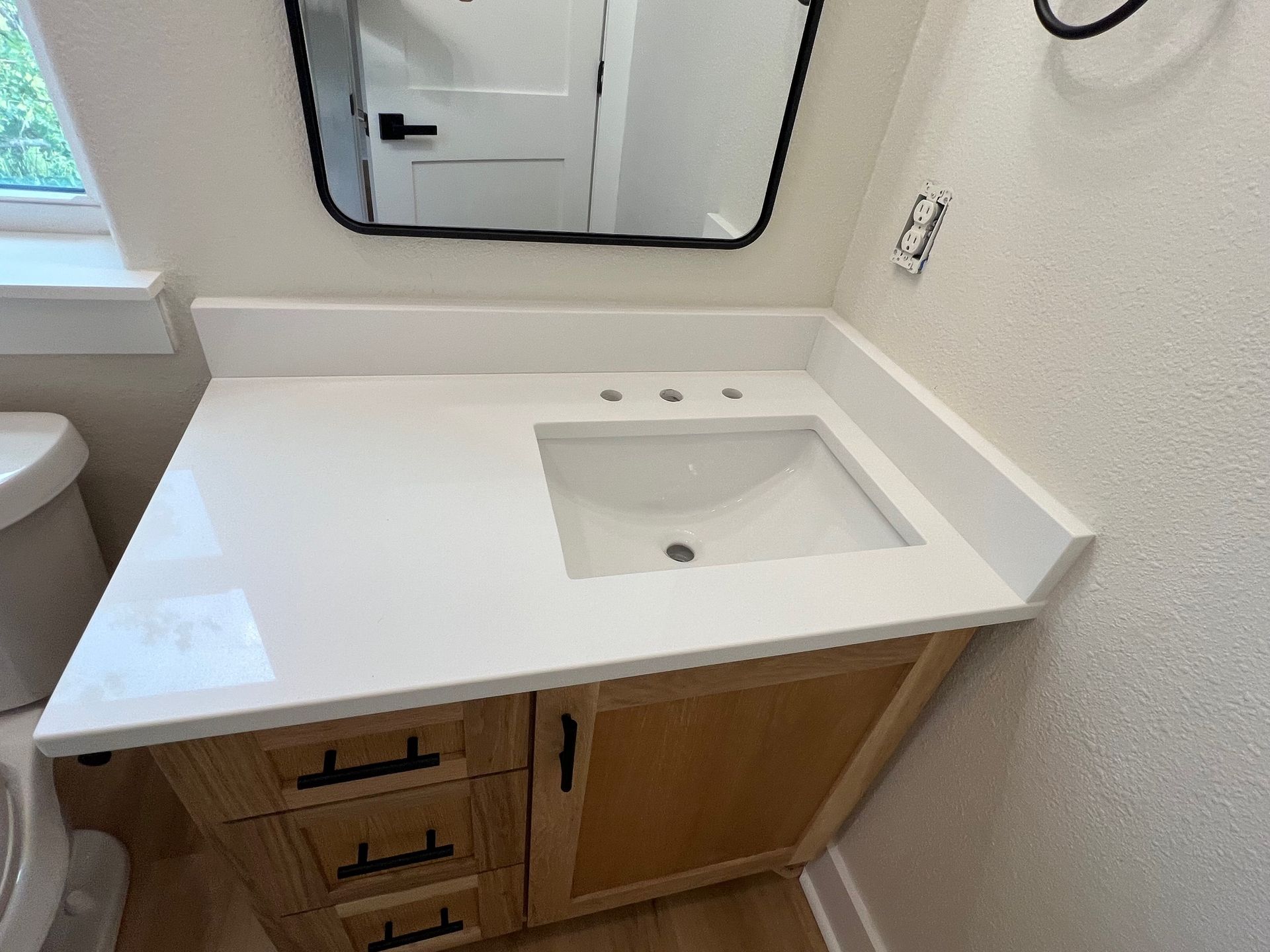 Modern bathroom vanity with white countertop, sink, mirror, and wood cabinet drawers