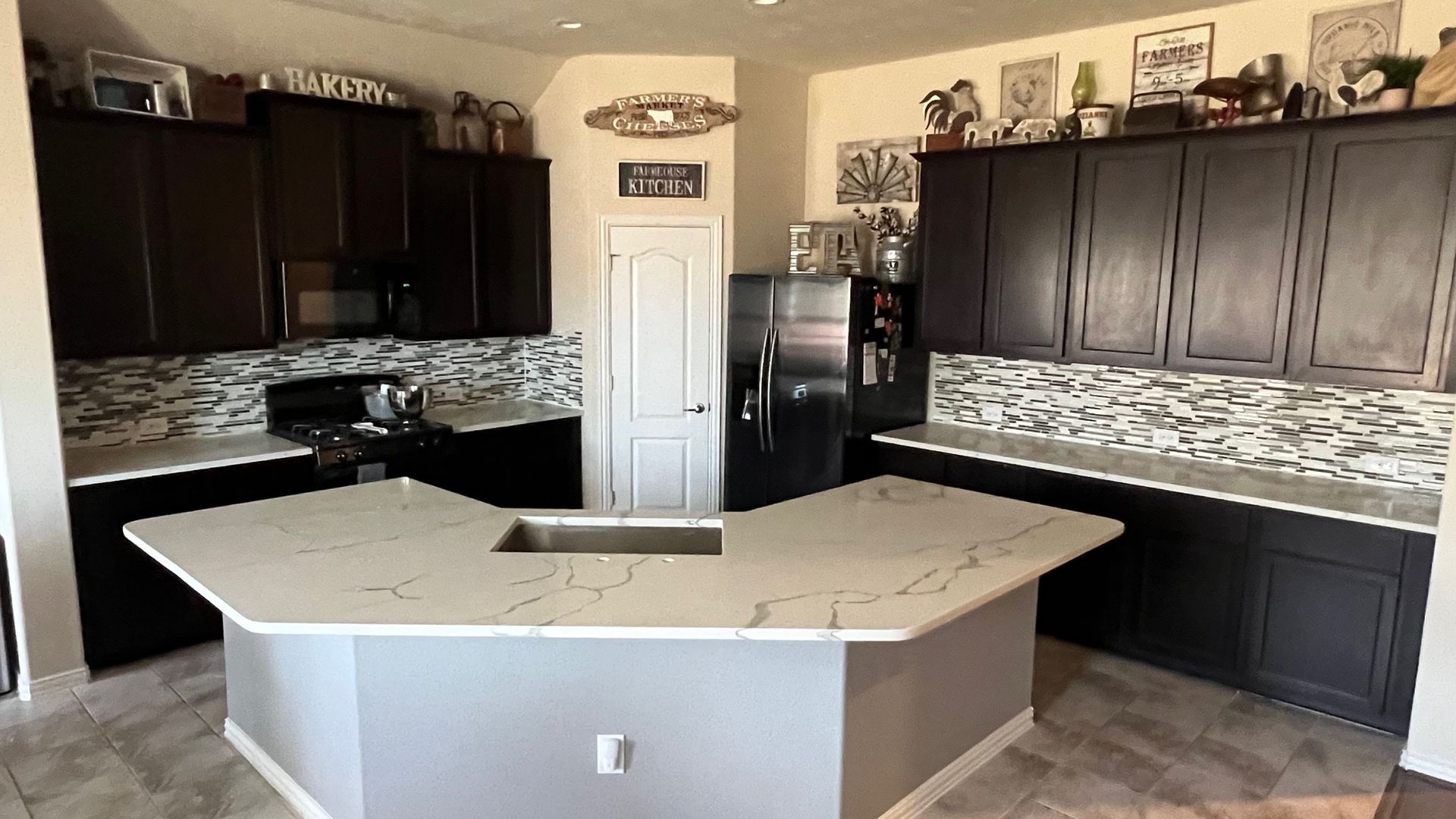 Modern kitchen with dark cabinets, light countertops, stainless appliances, and a large central island.